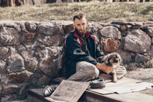 Poor homeless man with dog sitting on stairs outdoors