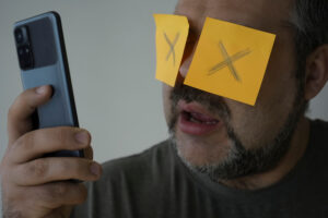 man addicted to smart phone with X's blocking his eyes
